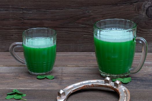 Shamrocks clovers on wooden table with a two mugs of green beer and a gold horseshoe. Background for St. Patrick's Day celebration