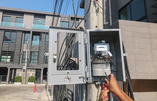 Electrician is setting up a meter to measure the electricity consumption in the box on the pole.