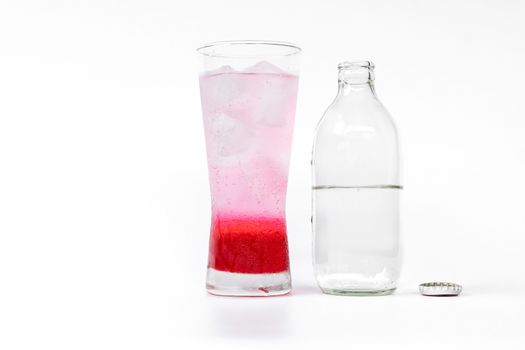 Glass of red nectar mixed with soda and soda bottles that open the lid on white background.