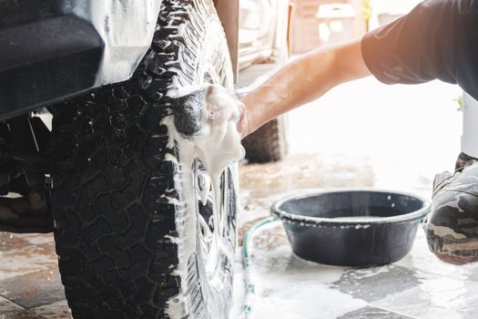 Car wash staff are using a sponge moistened with soap and water to clean the wheels of the car.