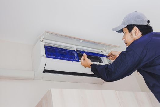 The air conditioning repairman in the blue uniform is removing the air filter for cleaning.