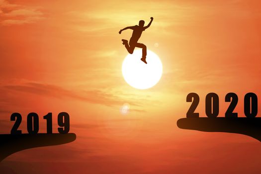 Silhouette of young business man jumping from the cliff that has the year number 2019 to the side that has the year number 2020 with sun rise background, Concept for new year target.