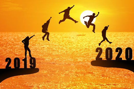 Silhouette group of young business mans jumping from the cliff that has the year number 2019 to the side that has the year number 2020 with sun rise background, Concept for new year target.