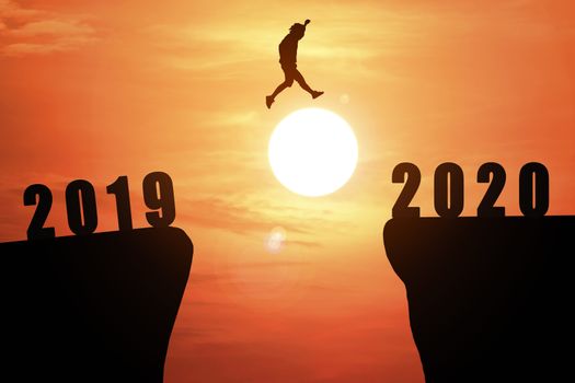 Silhouette of young business man jumping from the cliff that has the year number 2019 to the side that has the year number 2020 with sun rise background, Concept for new year target.