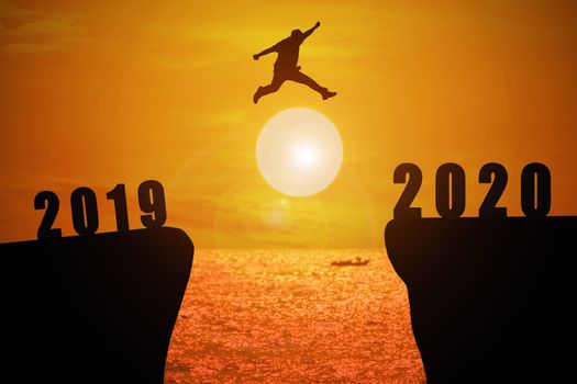 Silhouette of young business mans jumping from the cliff that has the year number 2019 to the side that has the year number 2020 with sun rise at the sea background, Concept for new year target.