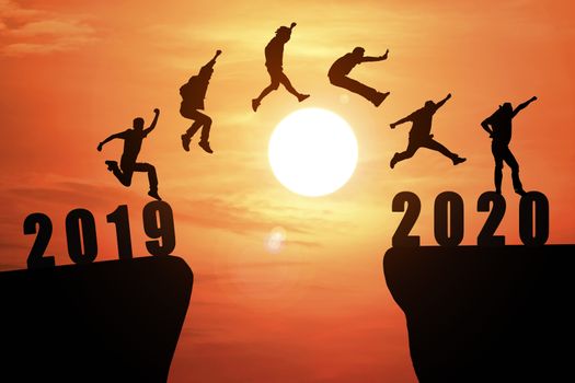 Silhouette group of young business mans jumping from the cliff that has the year number 2019 to the side that has the year number 2020 with sun rise background, Concept for new year target.