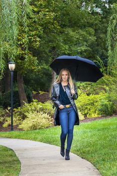 A gorgeous blonde model poses outdoors in her fall clothes while walking in a park