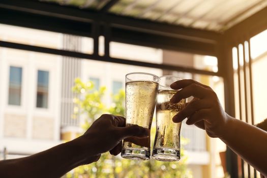 The hands of two men holding a glass of beer raised together to drink to celebrate the success.