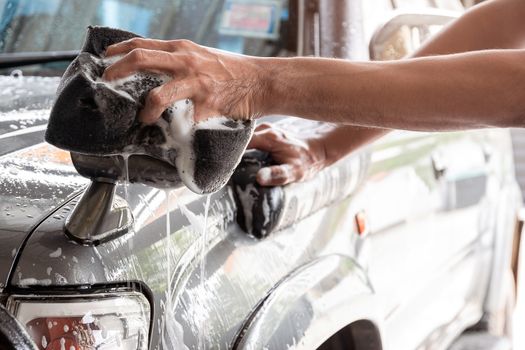 Car wash staff are using a sponge dampened with soap and water to clean the car.