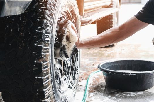 Car wash staff are using a sponge moistened with soap and water to clean the wheels of the car.