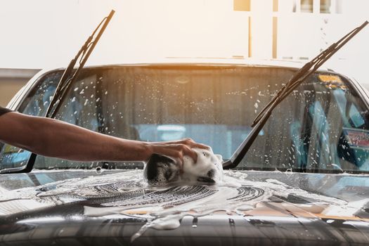 Car wash staff are using a sponge dampened with soap and water to clean the car.