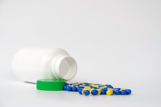 Closeup group of yellow and blue capsule medicine with plastic bottle on white background.