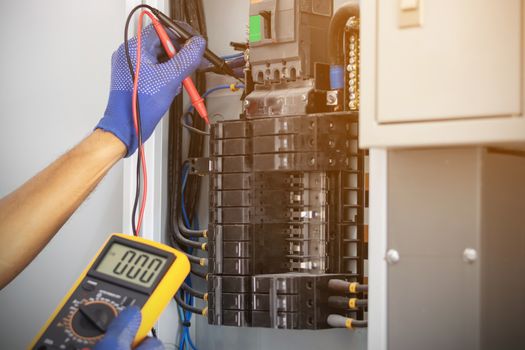 Electrician is using a digital meter to measure the voltage at the circuit breaker control cabinet on the wall.