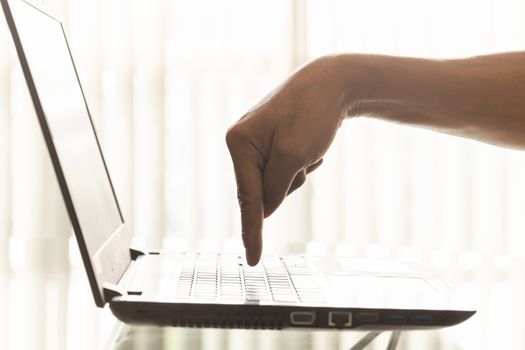 A businessman's finger is pressing down on the laptop's keyboard button in the office.