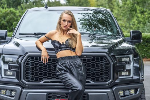 A gorgeous blonde model poses with a black truck on a fall day