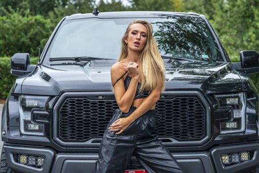 A gorgeous blonde model poses with a black truck on a fall day
