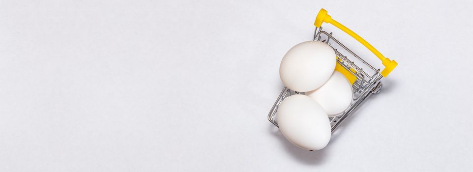 Fresh eggs in a shopping cart. Top view. Shopping, purchasing, and food delivery concept. White background. Close up shot. Isolated. Panorama, banner size with copy space.