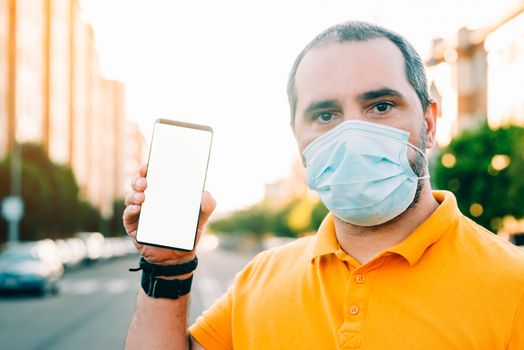 Portrait of 40s aged man with surgical medical mask standing, holding and showing smart phone display. medicine and health care concept.