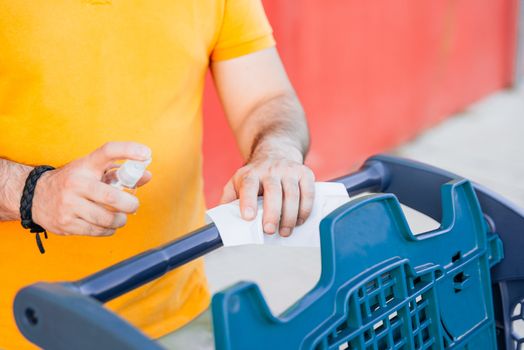 Man cleaning handle of shopping cart using antivirus antibacterial wet wipe.