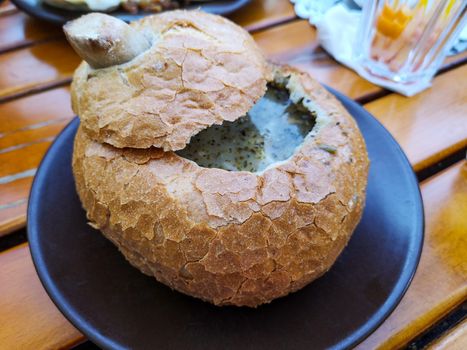 Soup in bread is a national dish of the Czech Republic. Mushroom soup puree in bread. Thick cream soup in bread On a dark plate on a wooden table.