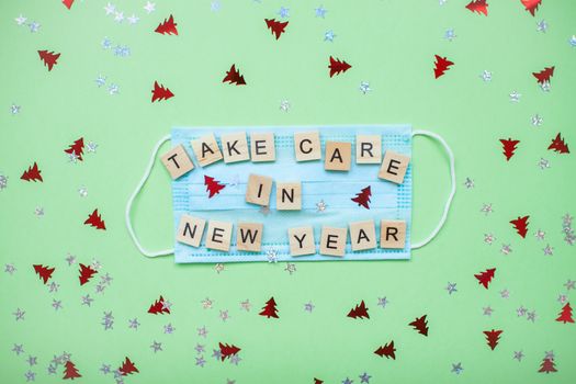 inscription from wooden blocks take care in new year on a medical protective mask and on a new year background