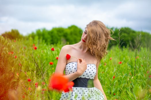 A young long-haired girl enjoys the colors of nature on a blooming poppy field on a hot summer day.