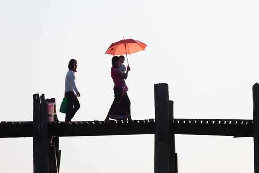 Local women walking on u bien bridge Mandalay Myanmar with child and red umbrella at sunset. High quality photo