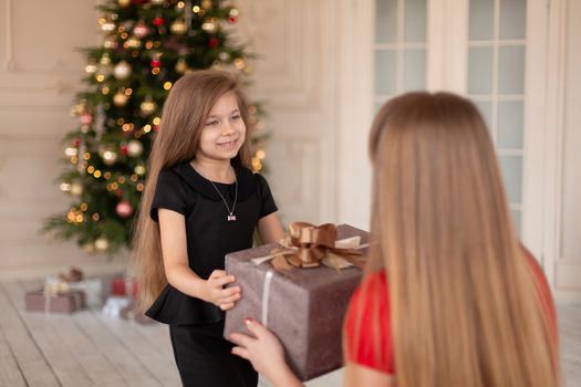 Little girl gives her mom a box with a Christmas present.