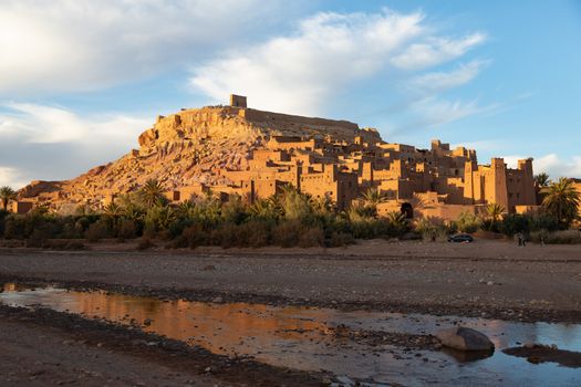 Ait Ben Haddou ksar Morocco, ancient fortress that is a Unesco Heritage site. Beautiful late afternoon light with honey, gold coloured mud brick construction with river and reflections in foreground the kasbah, or fortified town dates from 11th cent. and is on the former caravan route from the Sahara and Marrakech. The location has been used for many famous movies. High quality photo