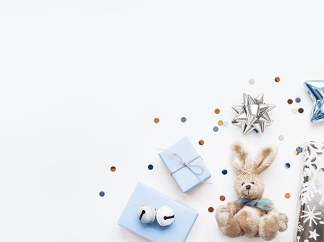 Holiday presents in shadows of blue - fluffy toy rabbit, gifts with decorative bells, sparkling confetti, decorative star. Gifts for little boy on Birthday.