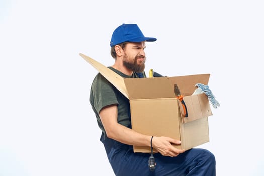 Worker man in uniform with a box in his hands tools delivery service light background. High quality photo