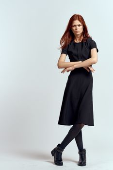 A woman in a black dress on a light background and pantyhose shoes red hair and pose in full growth. High quality photo