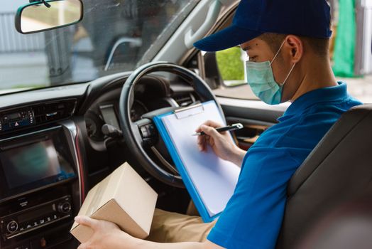 Asian delivery courier young man driver inside the van car with parcel post boxes checking amount he protective face mask, under curfew quarantine pandemic coronavirus COVID-19