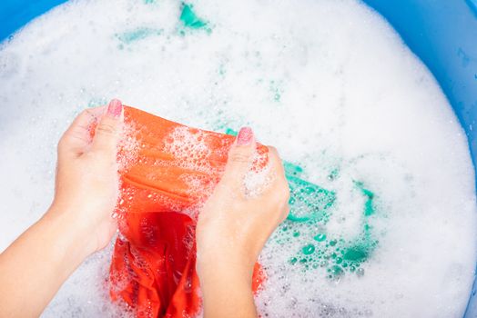 Closeup young Asian woman use hands washing color clothes in basin with detergent have soapy bubble water, studio shot background, laundry concept