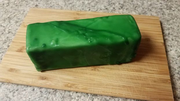 cheese encased or sealed in green wax on wood cutting board