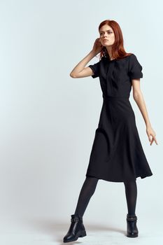 A woman in a black dress on a light background and pantyhose shoes red hair and pose in full growth. High quality photo