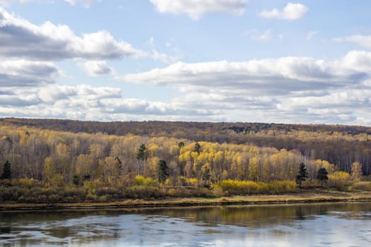 Beautiful, wide river autumn among the woods. Calm and quiet place with autumn colors. Reflection of clouds and forests in water in good weather