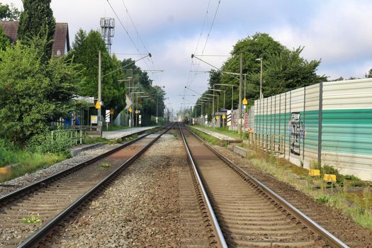 Railway tracks with a small train station, noise protection wall and trees in the background
