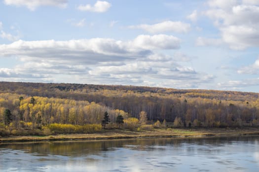 Beautiful, wide river autumn among the woods. Calm and quiet place with autumn colors. Reflection of clouds and forests in water in good weather