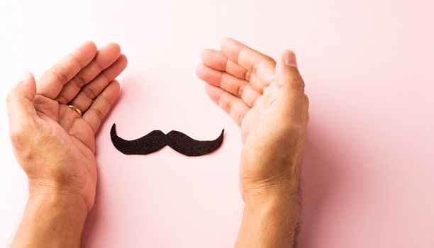 The man uses hand holding black mustache, studio shot isolated on white background, Prostate cancer awareness month, Fathers day, minimal November moustache concept