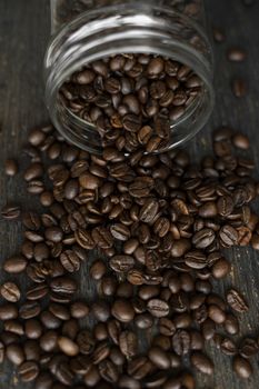 Roasted fresh arabica coffee beans scattered on a table from a little jar on a wooden table. Fresh coffee beans