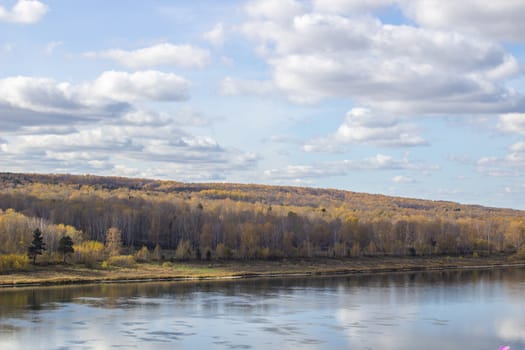 Beautiful, wide river autumn among the woods. Calm and quiet place with autumn colors. Reflection of clouds and forests in water in good weather