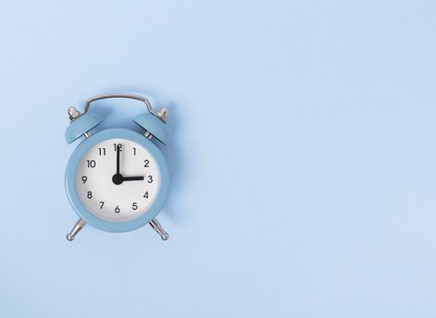 Retro alarm clock on blue background. Monochrome simple flat lay with copy space. Time concept. Stock photography.