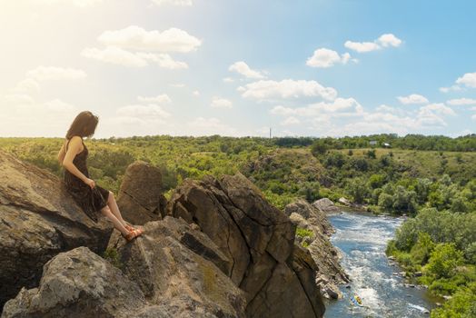 A young woman sits on a rock and looks at a picturesque landscape of the southern bug river. Bug Guard national nature park in Ukraine. Stock photography.