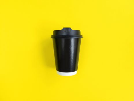 Black paper coffee cup to go on yellow backgroud. Flat lay style. Minimal concept. Stock photography.