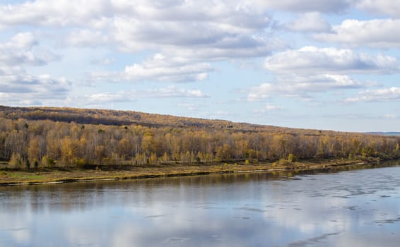 Beautiful, wide river autumn among the woods. Calm and quiet place with autumn colors. Reflection of clouds and forests in water in good weather