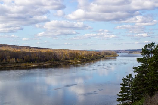 Beautiful, wide river autumn among the woods. Calm and quiet place with autumn colors. Reflection of clouds and forests in water in good weather