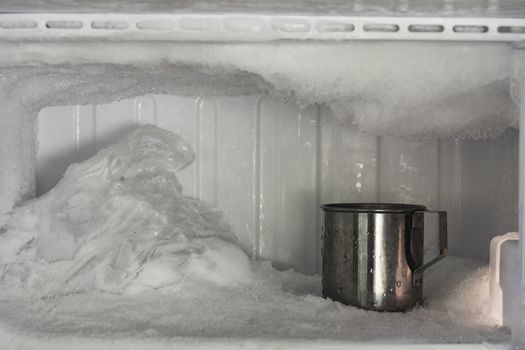 Stainless steel drinking water glass in freezer of a refrigerator. Ice buildup inside of a freezer walls.