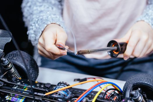 A young girl learns how to solder and is attaching an ESC to a motor in an RC car at a home workshop