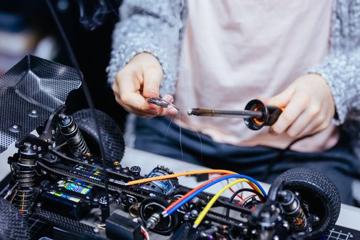 A young girl learns how to solder and is attaching an ESC to a motor in an RC car at a home workshop